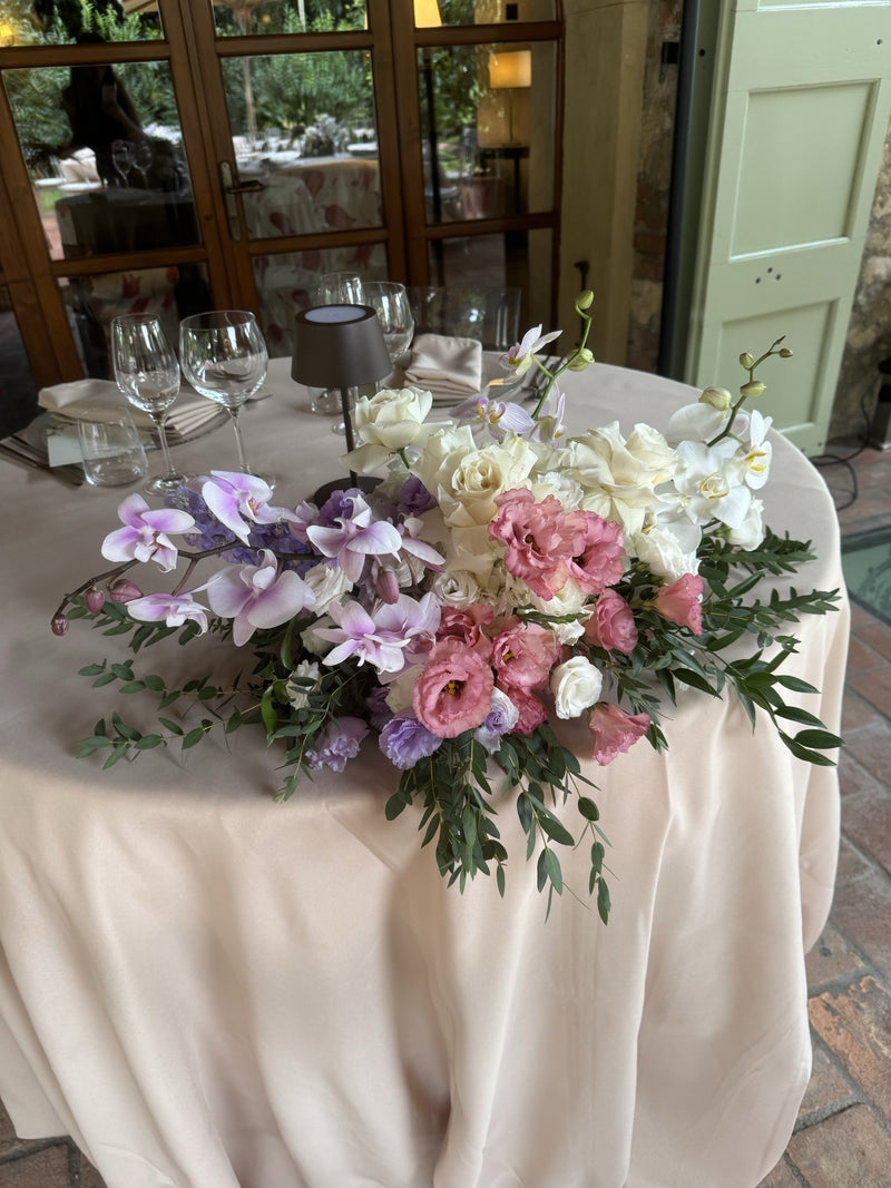 Centrotavola con orchidee, lisianthus e rose bianche sul tavolo degli sposi