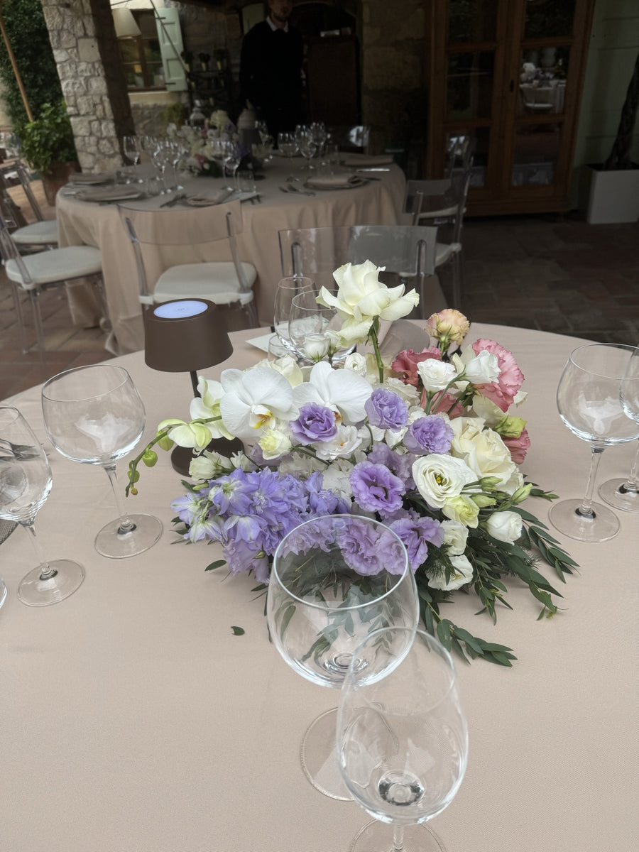 Centrotavola lilla e bianco con orchidee e delphinium su tavolo rotondo